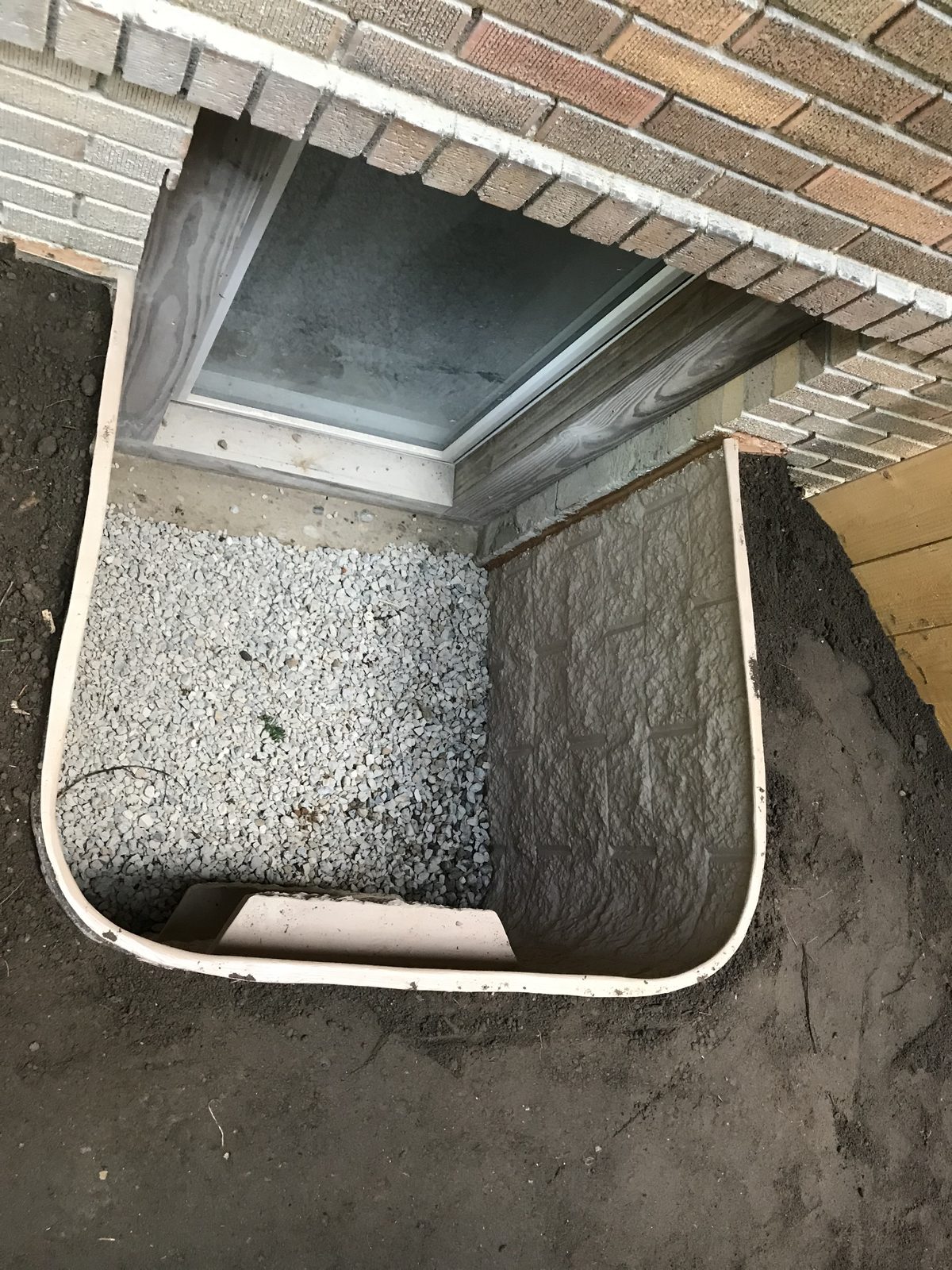 Top-down view of an egress window well with gravel drainage base